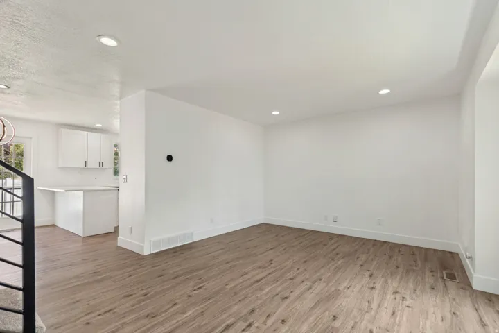 Spacious living area featuring contemporary wood-finish flooring, recessed lighting, and crisp white walls