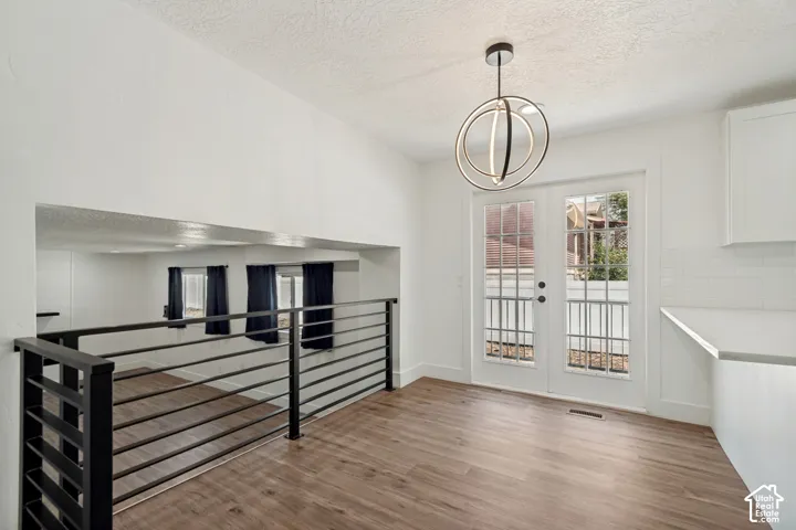 Open-concept dining area with wood-finish flooring, a contemporary chandelier, and French doors