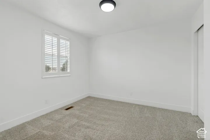 Neutral wall paint with textured carpeting, a flush mount ceiling light fixture, and a window with plantation shutters