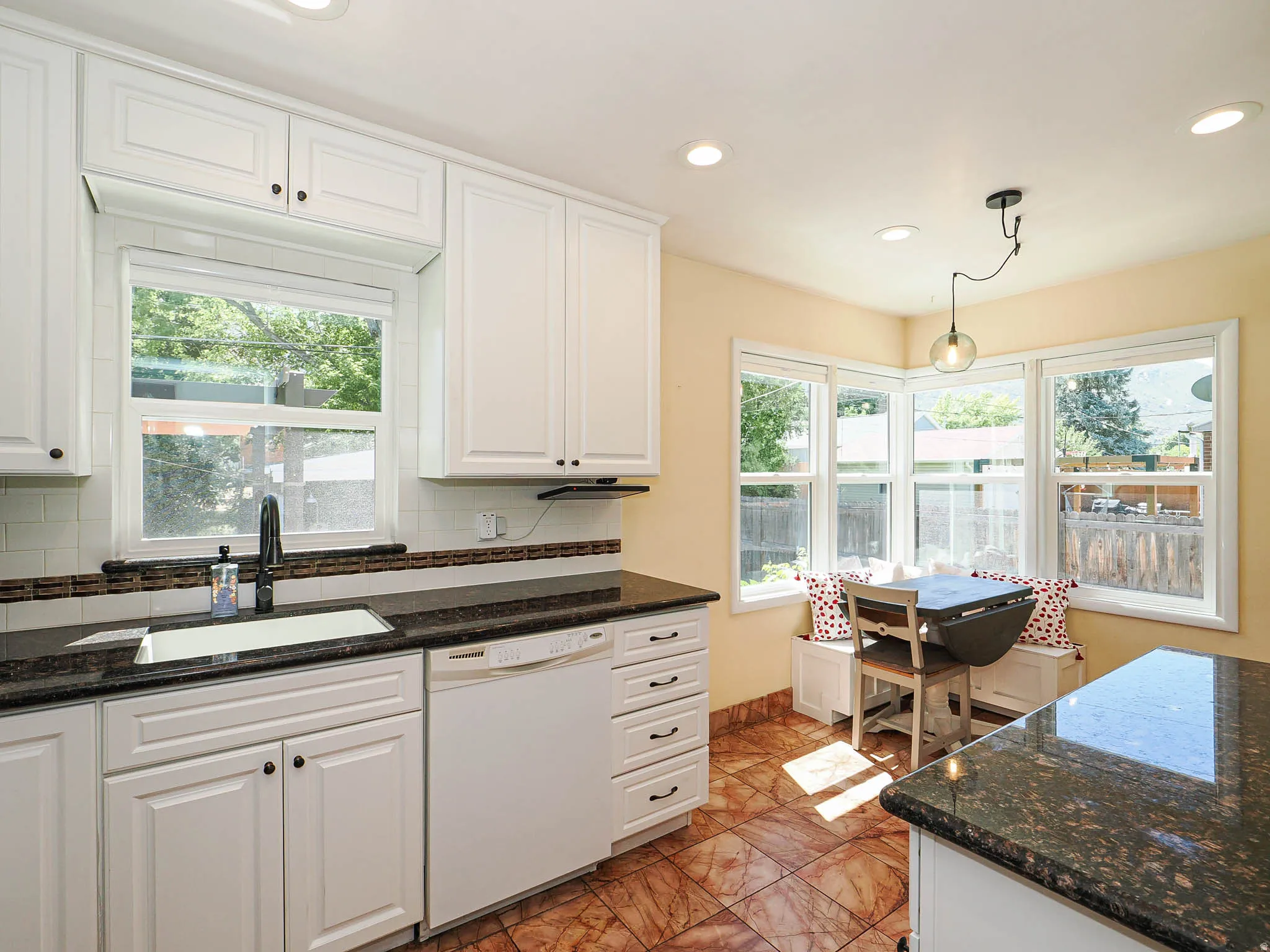 Kitchen featuring white cabinetry with dark hardware, dark granite countertops, a white subway tile backsplash, and a built-in banquette seating area with multiple windows