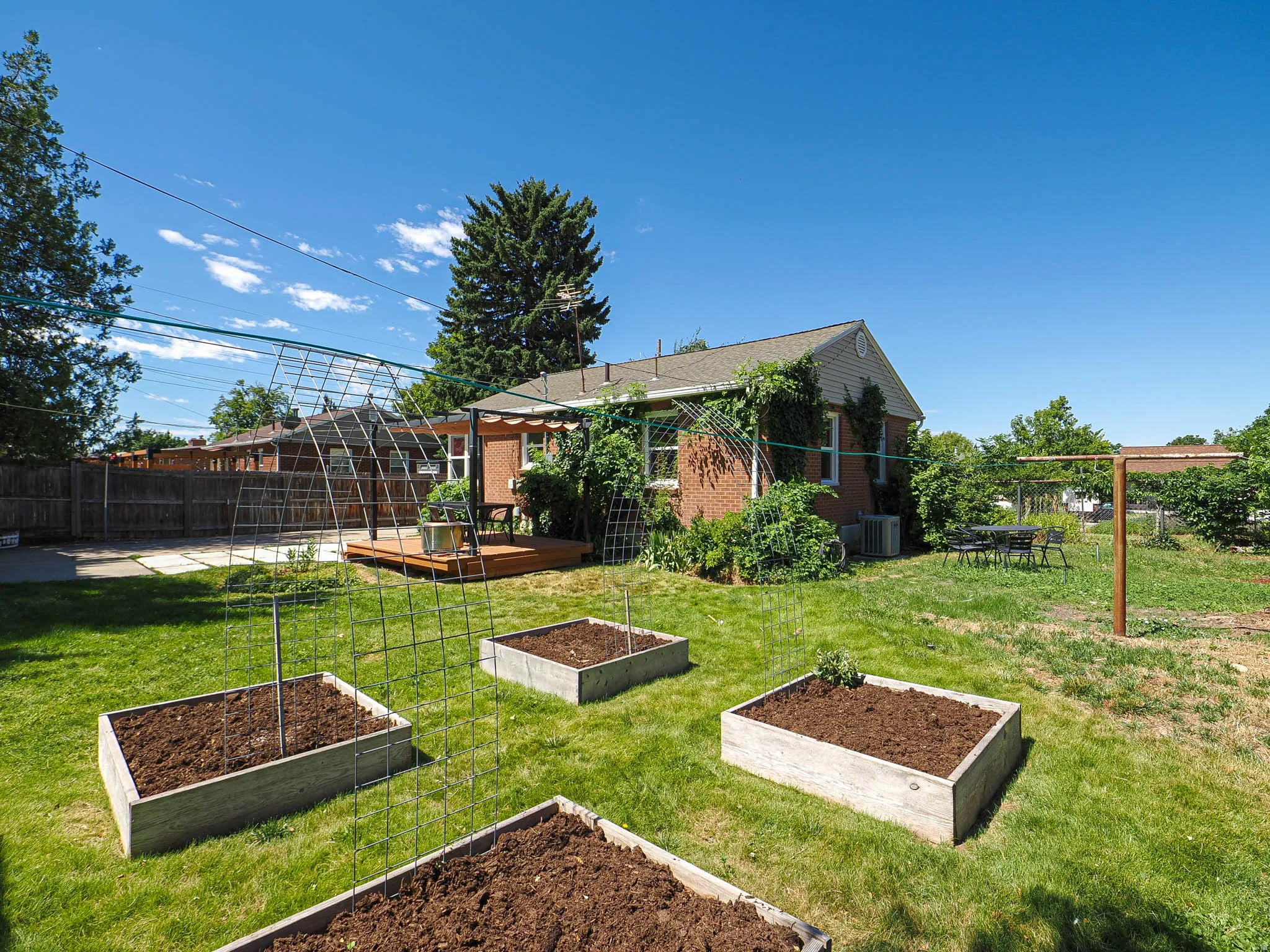 Expansive backyard featuring three raised garden beds, a wood-deck patio, and a brick-sided exterior with mature landscaping