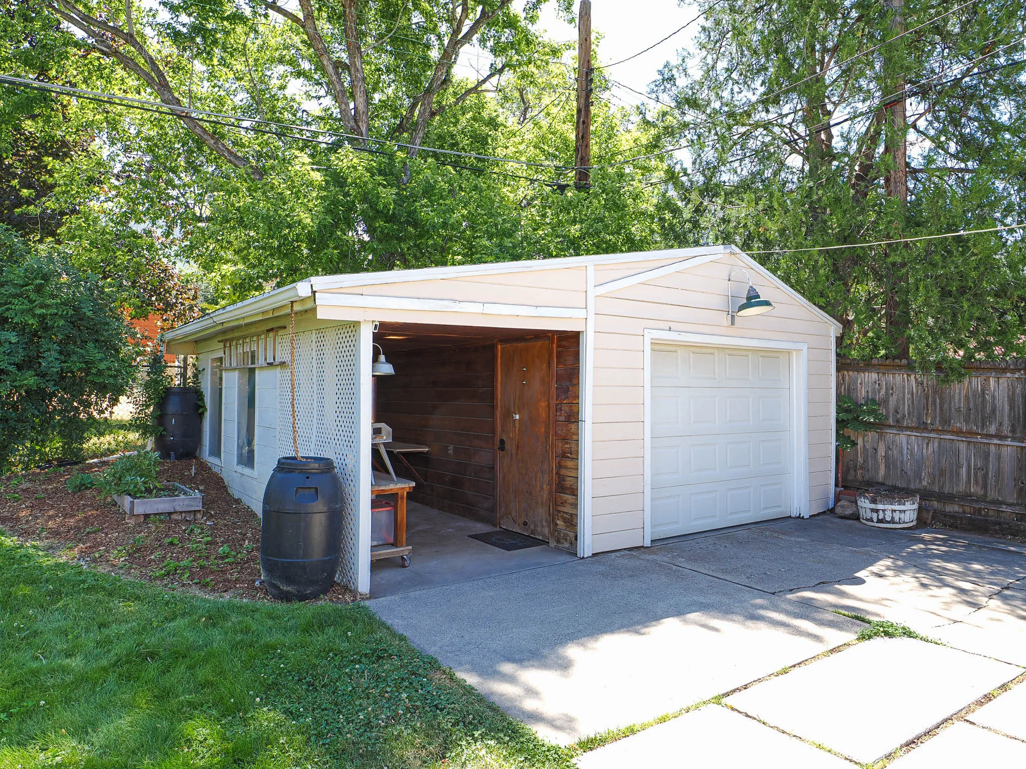 Detached garage with a single roll-up door, horizontal siding, and an attached covered carport featuring a wood-paneled wall
