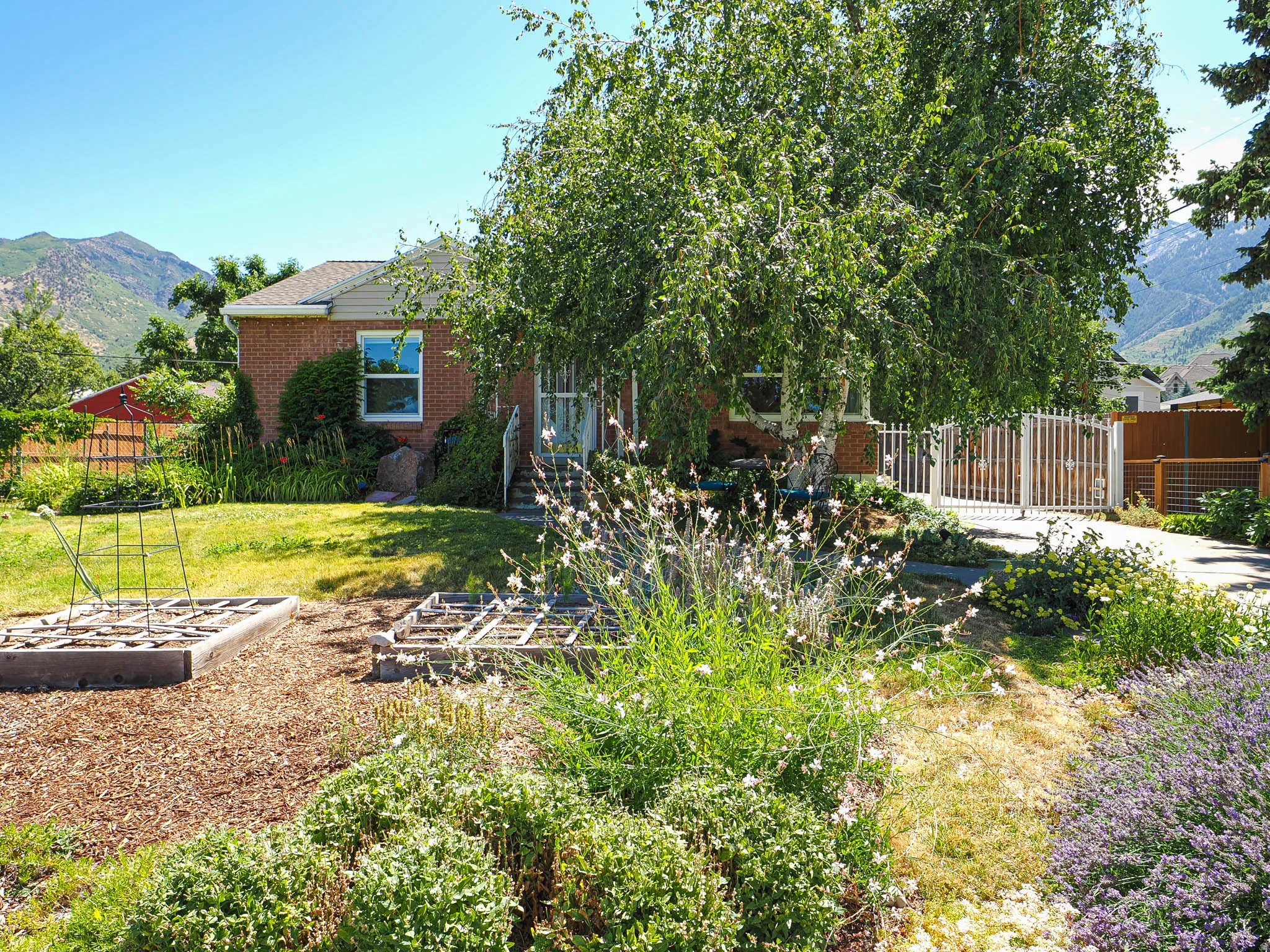 Brick exterior with a peaked roofline, front lawn, mature trees, and a mountain backdrop