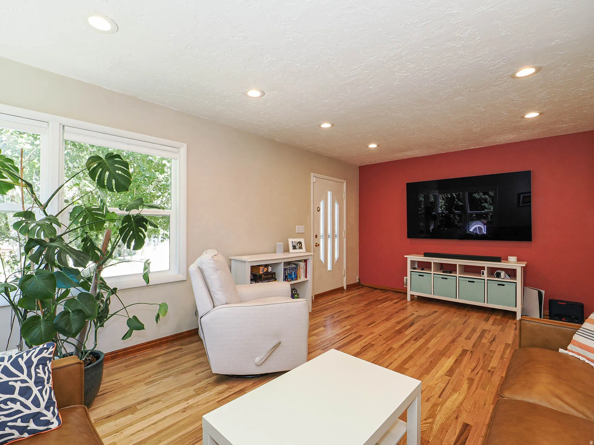 Hardwood flooring throughout, recessed ceiling lighting, a large window, a white entry door with decorative glass inserts, and an accent wall