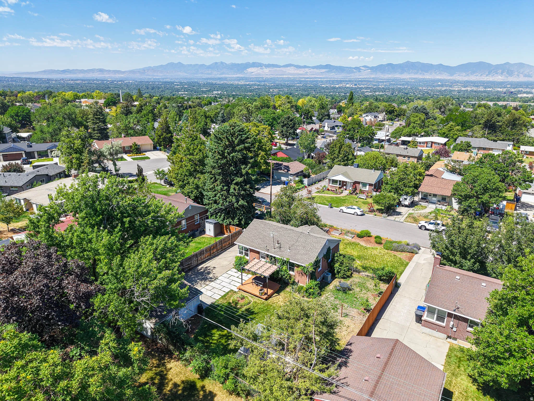 Property exterior featuring a wood deck with pergola, concrete paver patio, mature trees, and a mountain backdrop