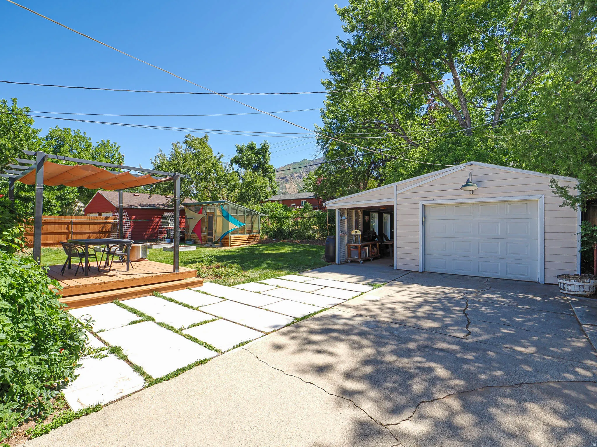 Expansive backyard featuring a detached garage with an attached carport, a wood-finish deck with a pergola, a concrete paver patio, and mature trees