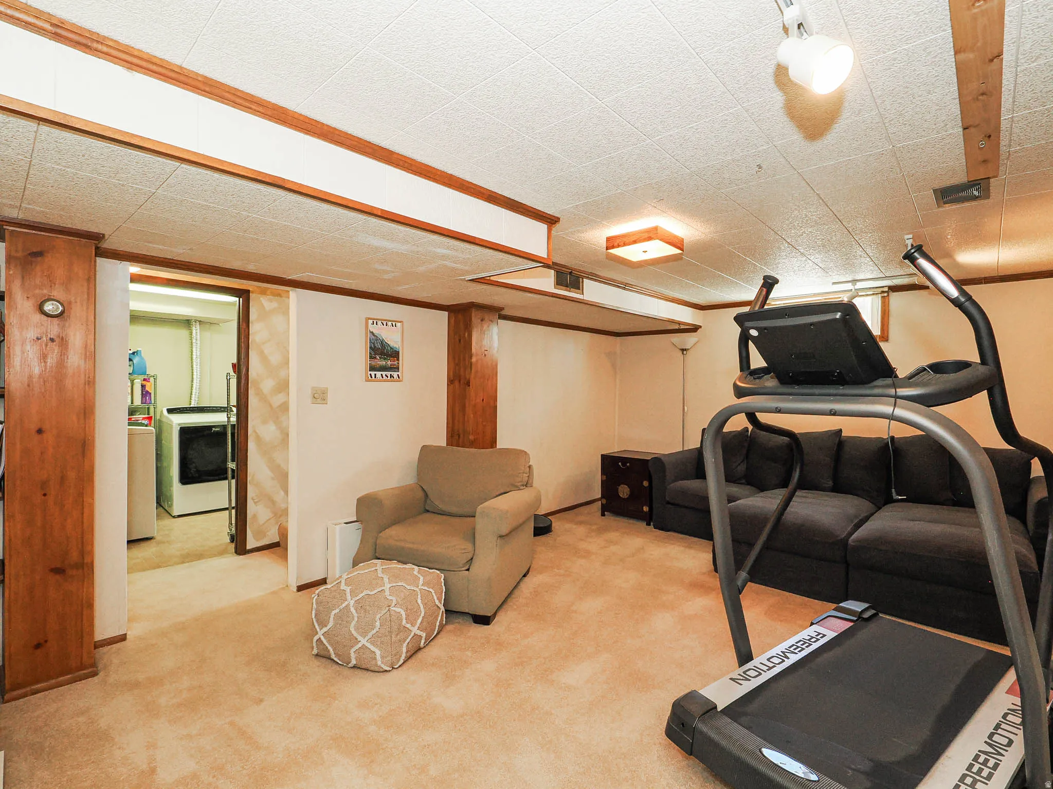Carpeted recreational area featuring white walls, wood trim, and a drop ceiling with integrated lighting