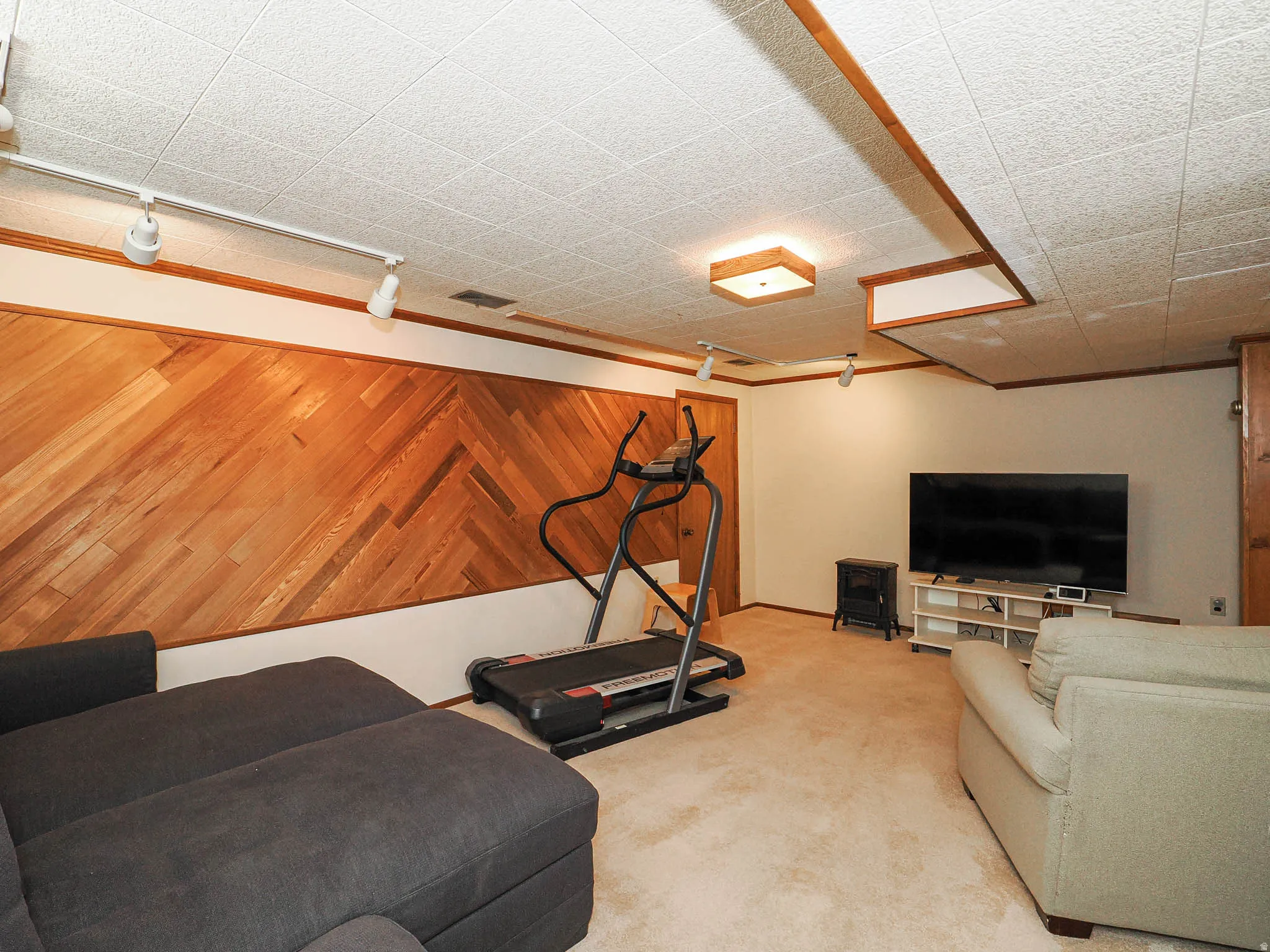 Wood-paneled accent wall with a herringbone pattern, track lighting, and a drop ceiling