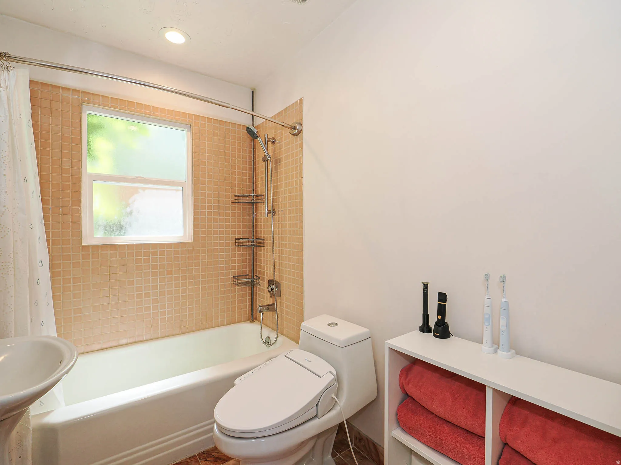 Bathroom featuring a pedestal sink, white bathtub, and mosaic tile shower surround