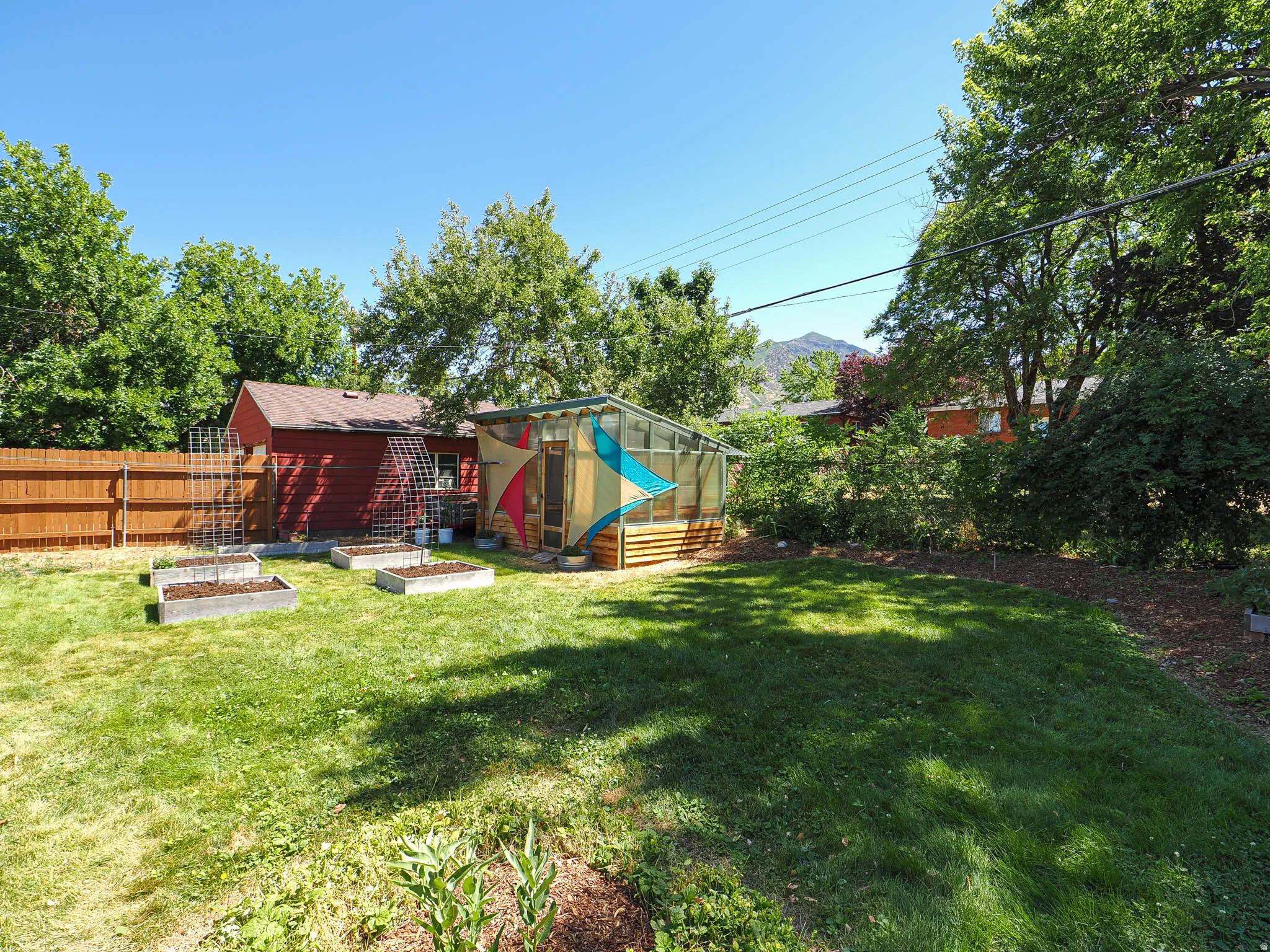 Expansive backyard featuring a greenhouse with wood-finish siding, a red storage shed, and multiple raised garden beds