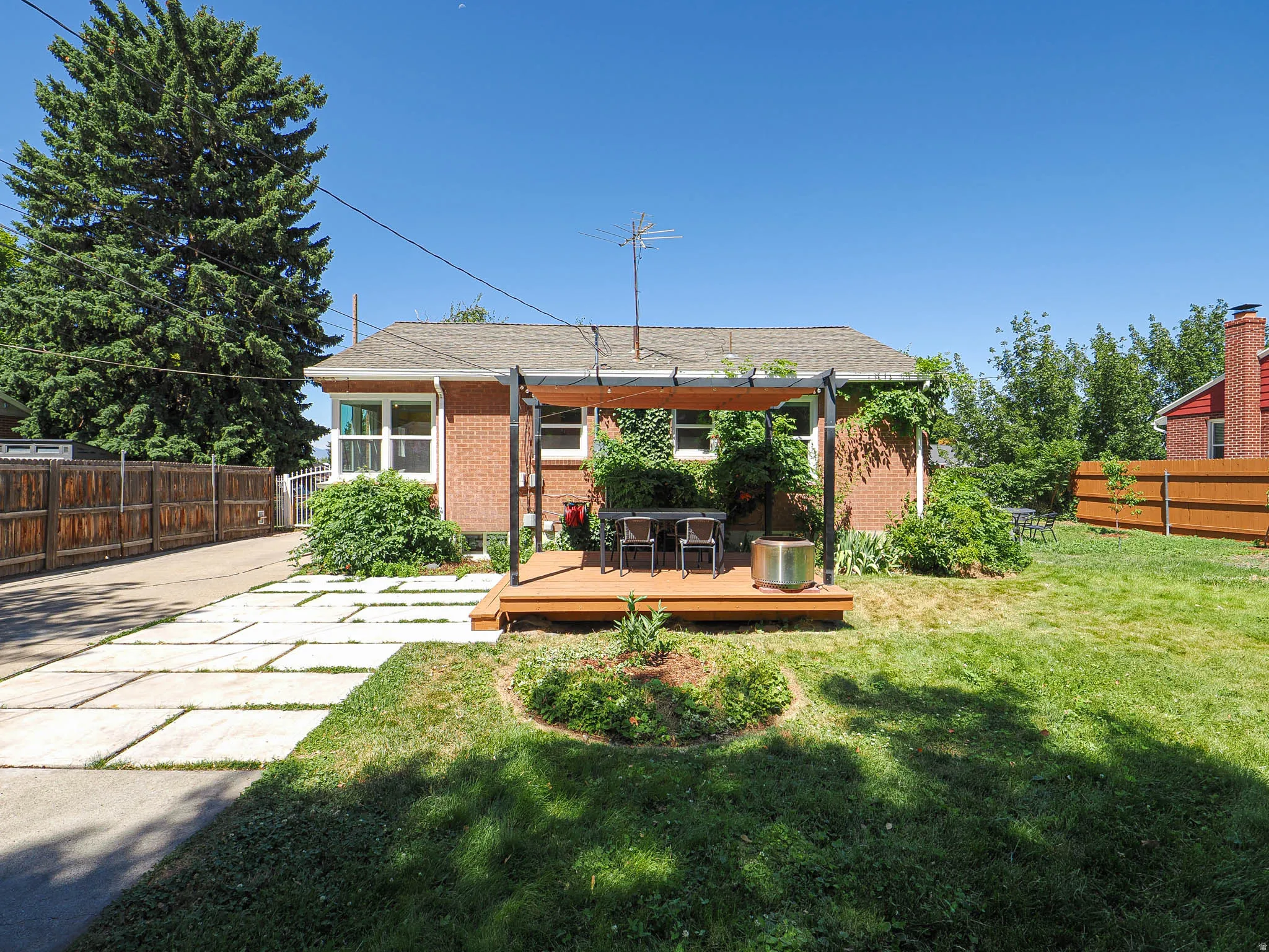 Rear brick exterior featuring a wood deck with a pergola, a spacious lawn, and a modern patio paver walkway