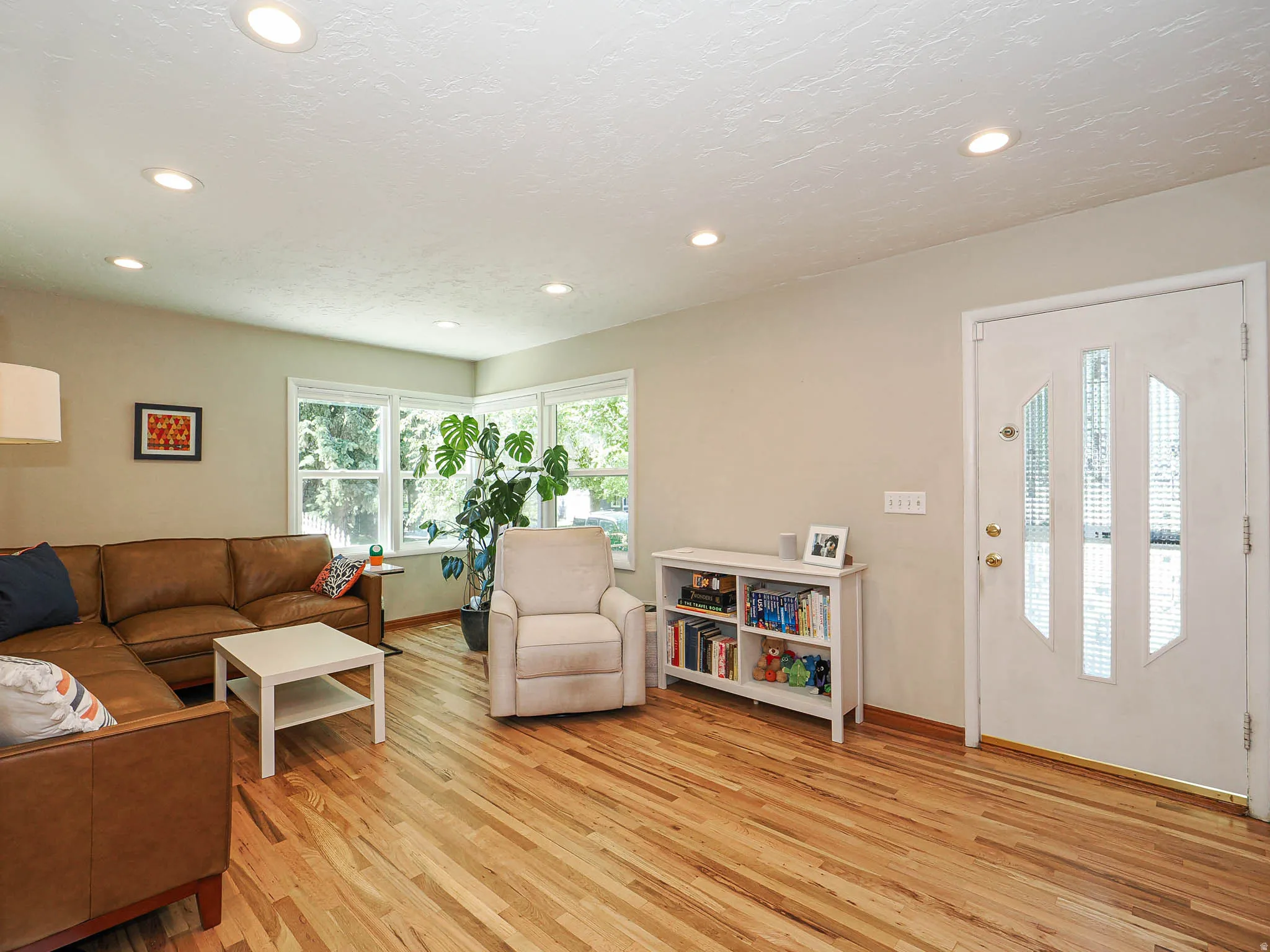 Hardwood flooring spans this living area, featuring recessed lighting, multiple windows, and a glass-paneled entry door