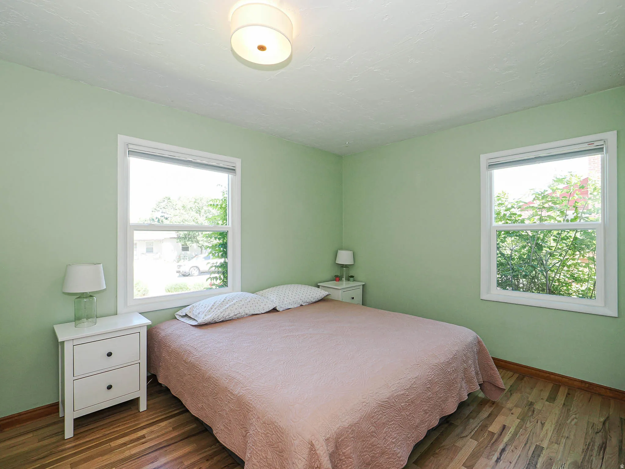 Bedroom featuring two windows with white frames, light green painted walls, and wood-finish flooring