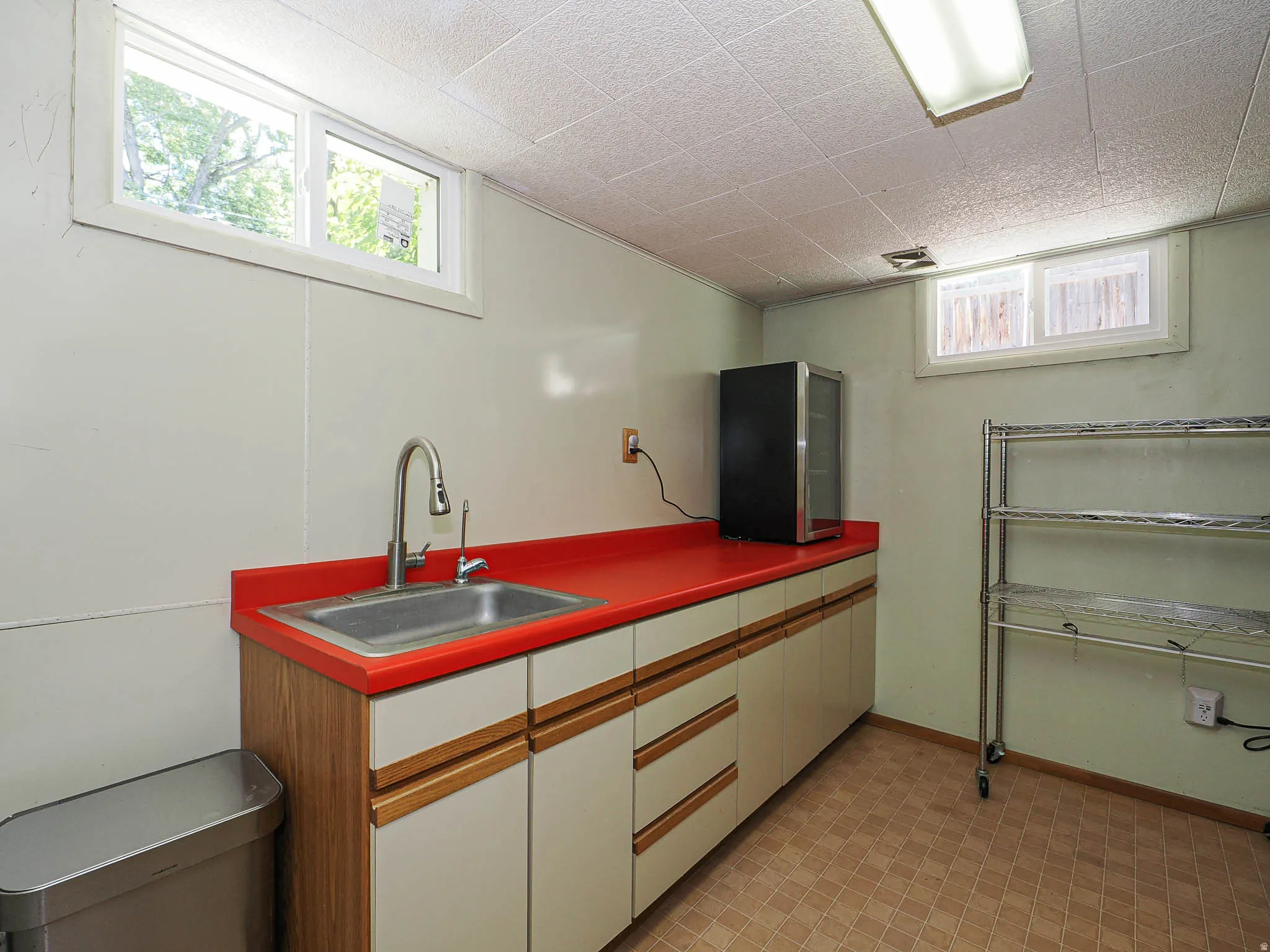 Utility area featuring a red countertop with an undermount sink, wood-finish cabinetry, and tiled flooring