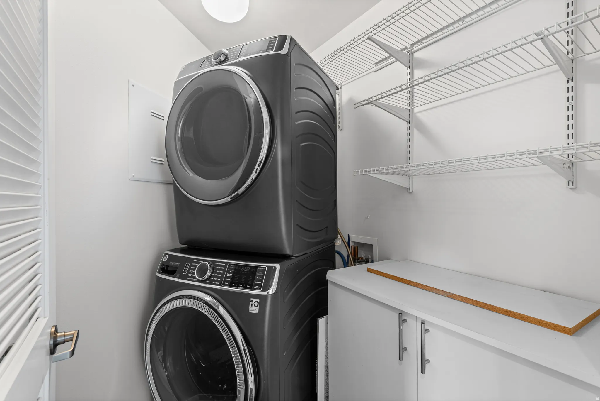 Dedicated laundry space featuring a stacked washer and dryer unit, extensive wire shelving, a built-in base cabinet, and a bright overhead light fixture