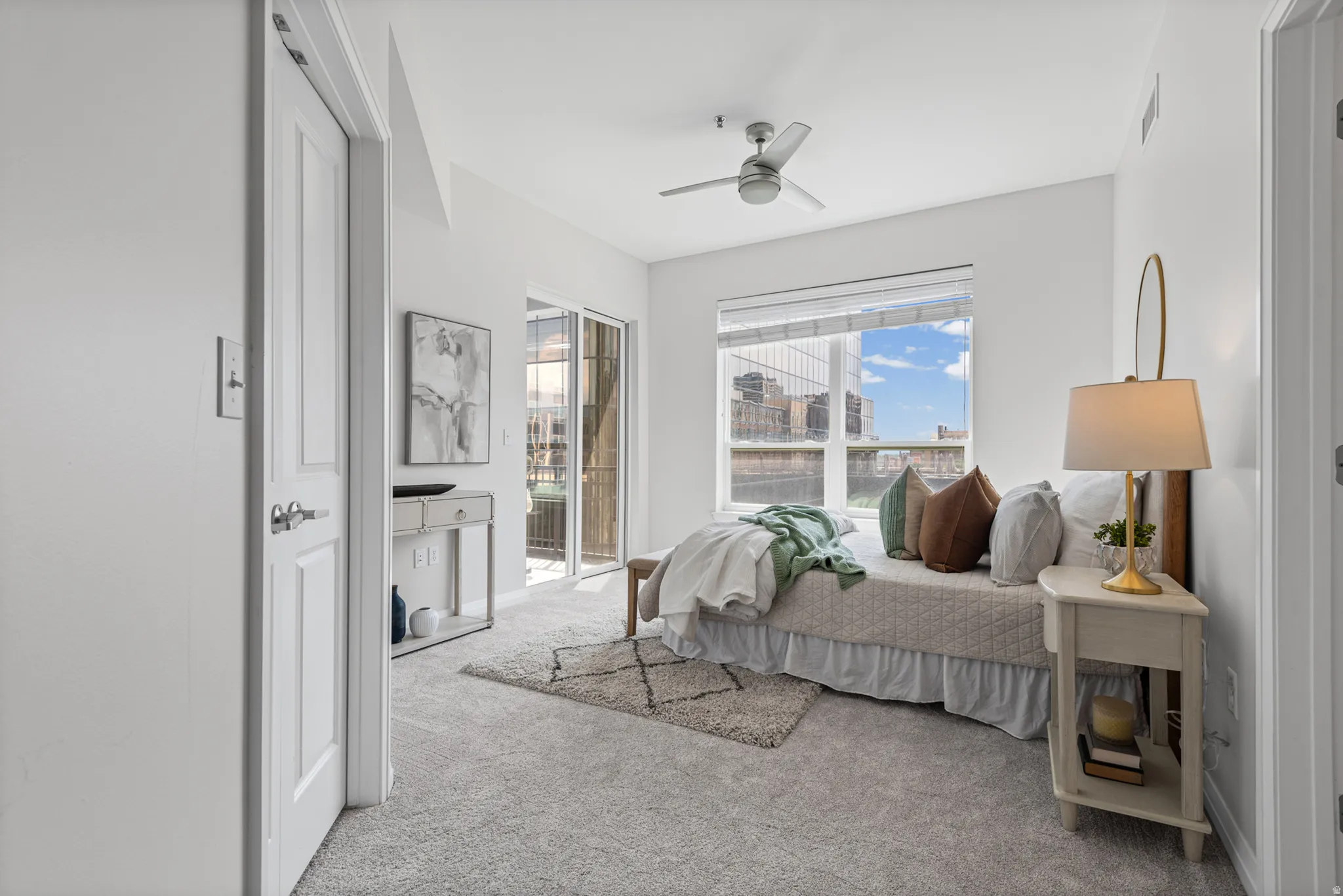 Carpeted interior space featuring a large window with blinds, a sliding glass door to an exterior balcony, a ceiling fan, and white paneled doors
