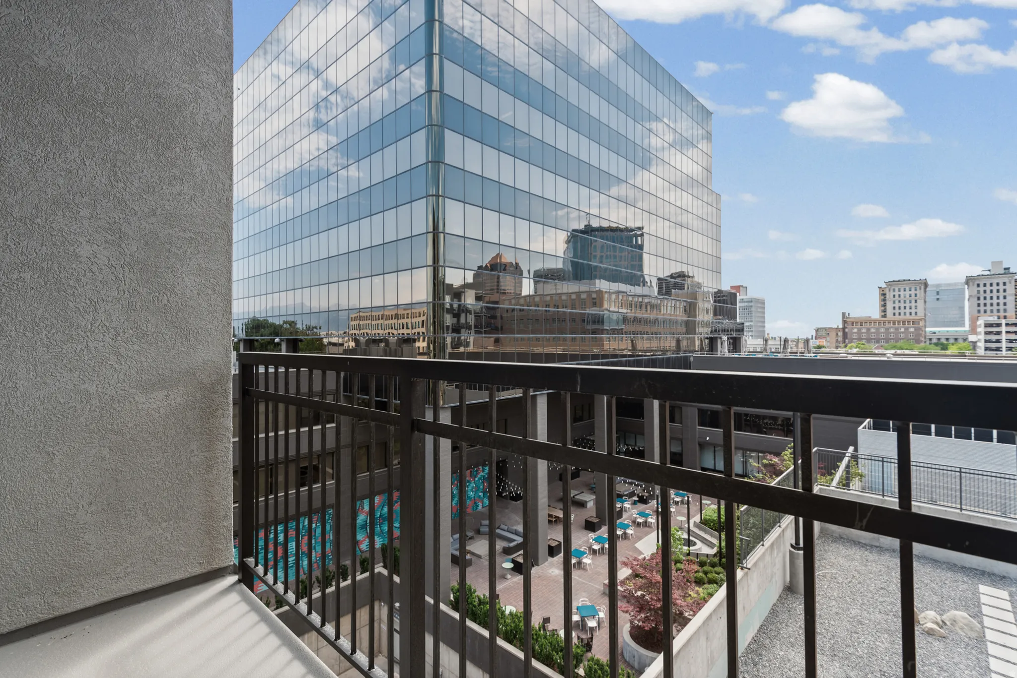 Balcony with metal railings overlooking a common area courtyard and an adjacent glass-exterior building