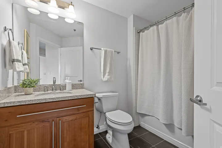 Bathroom featuring a wood-finish vanity with a light speckled countertop, an undermount sink, and a large wall-mounted mirror