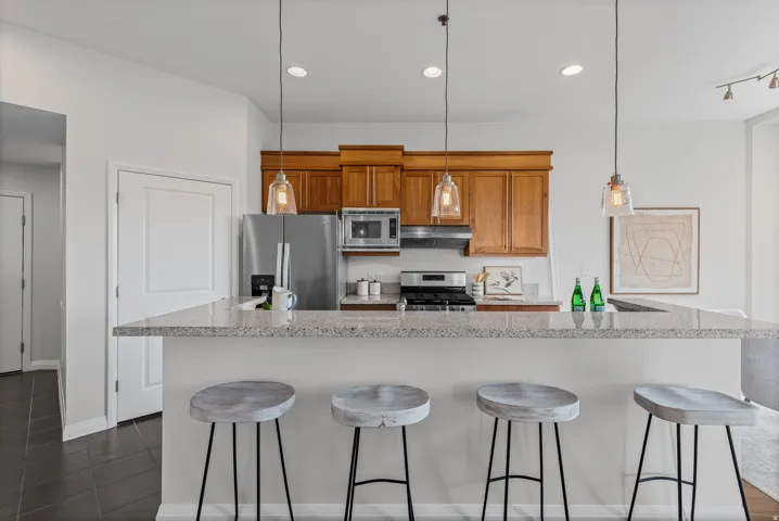 Kitchen featuring a spacious peninsula with a light-toned countertop, stainless steel appliances, wood cabinetry, and pendant lighting