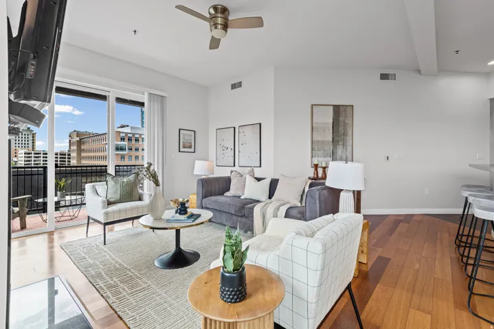 Open-concept living area featuring wood-finish flooring, a ceiling fan, and abundant natural light from the balcony's sliding glass doors