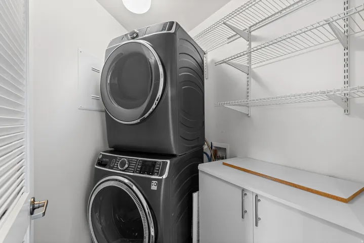 Dedicated laundry space featuring a stacked washer and dryer unit, extensive wire shelving, a built-in base cabinet, and a bright overhead light fixture