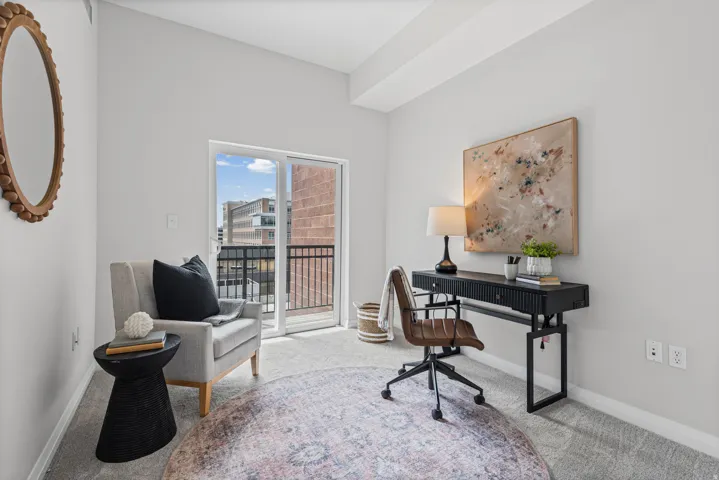 Light-filled room featuring a sliding glass door opening to a private balcony, neutral carpeting, and contemporary wall finishes
