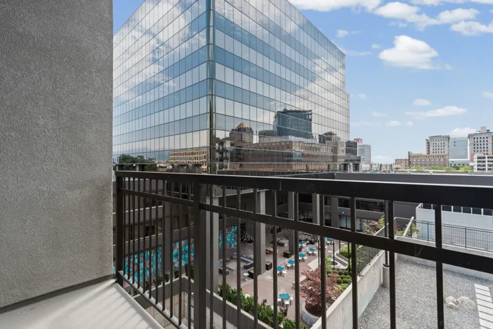 Balcony with metal railings overlooking a common area courtyard and an adjacent glass-exterior building