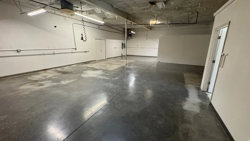 Open commercial space featuring concrete flooring, white walls, exposed conduit, and fluorescent lighting fixtures