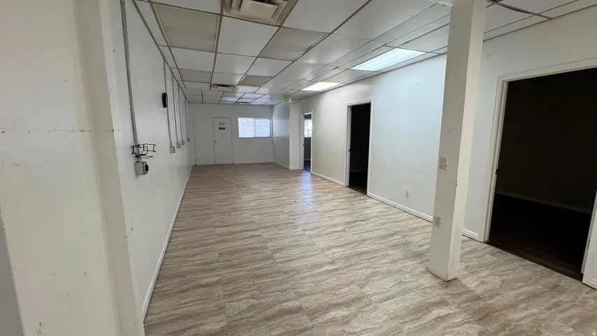 Spacious interior featuring neutral-toned tile flooring, drop ceiling with recessed lighting, multiple doorways, and exposed conduit on the perimeter wall