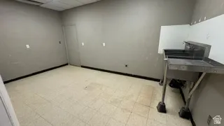 Room featuring a stainless steel utility sink with dual basins, tile flooring, grey painted walls, black baseboards, and a dropped ceiling with panel lighting