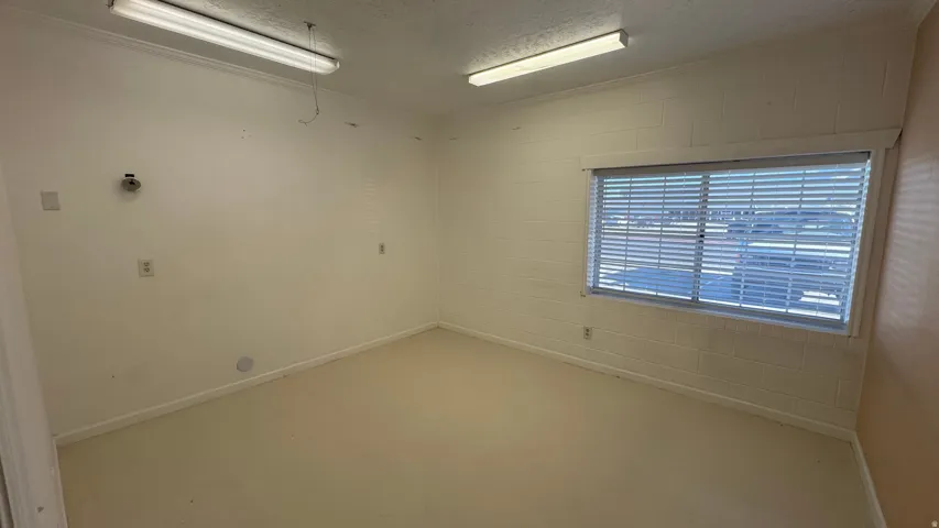 Spacious interior room with light-toned flooring, white painted walls, and a large window fitted with horizontal blinds