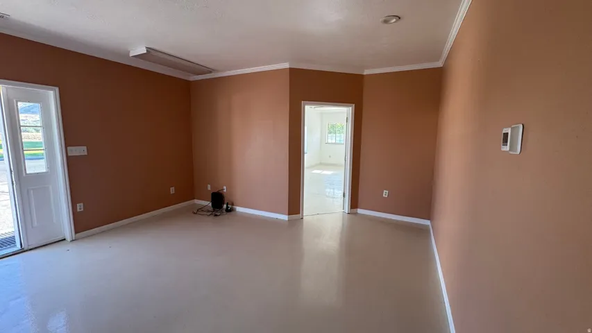 Spacious interior room with light-colored flooring, earth-toned walls, and white crown molding