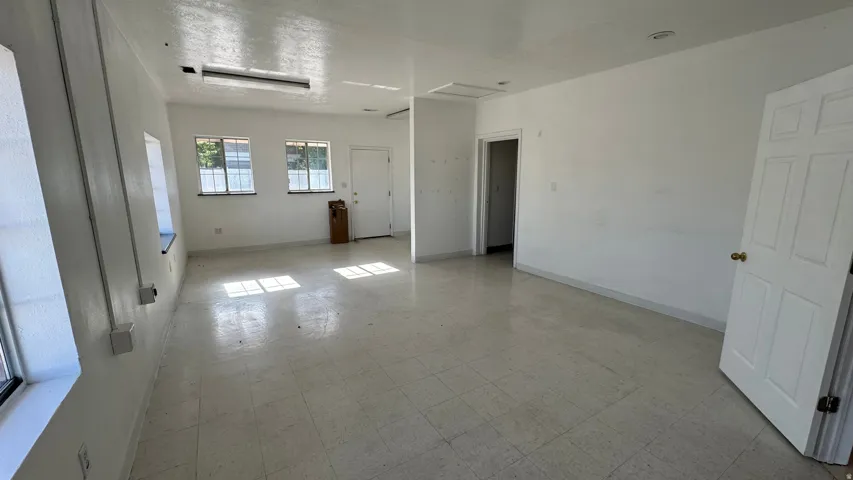 Spacious room with white walls, multiple windows, recessed lighting, tile flooring, and a white paneled door