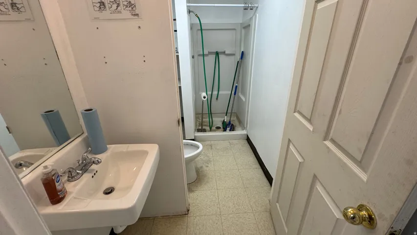 Bathroom featuring a wall-mounted sink with a chrome faucet, a rectangular mirror, a shower stall, and light-toned floor tiling