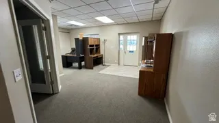 Open concept office area featuring neutral-toned walls, gray carpeting, and a white acoustical tile ceiling