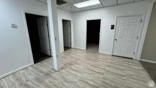 Spacious interior featuring wood-finish flooring, white painted walls, multiple paneled doors, and a suspended ceiling with integrated lighting