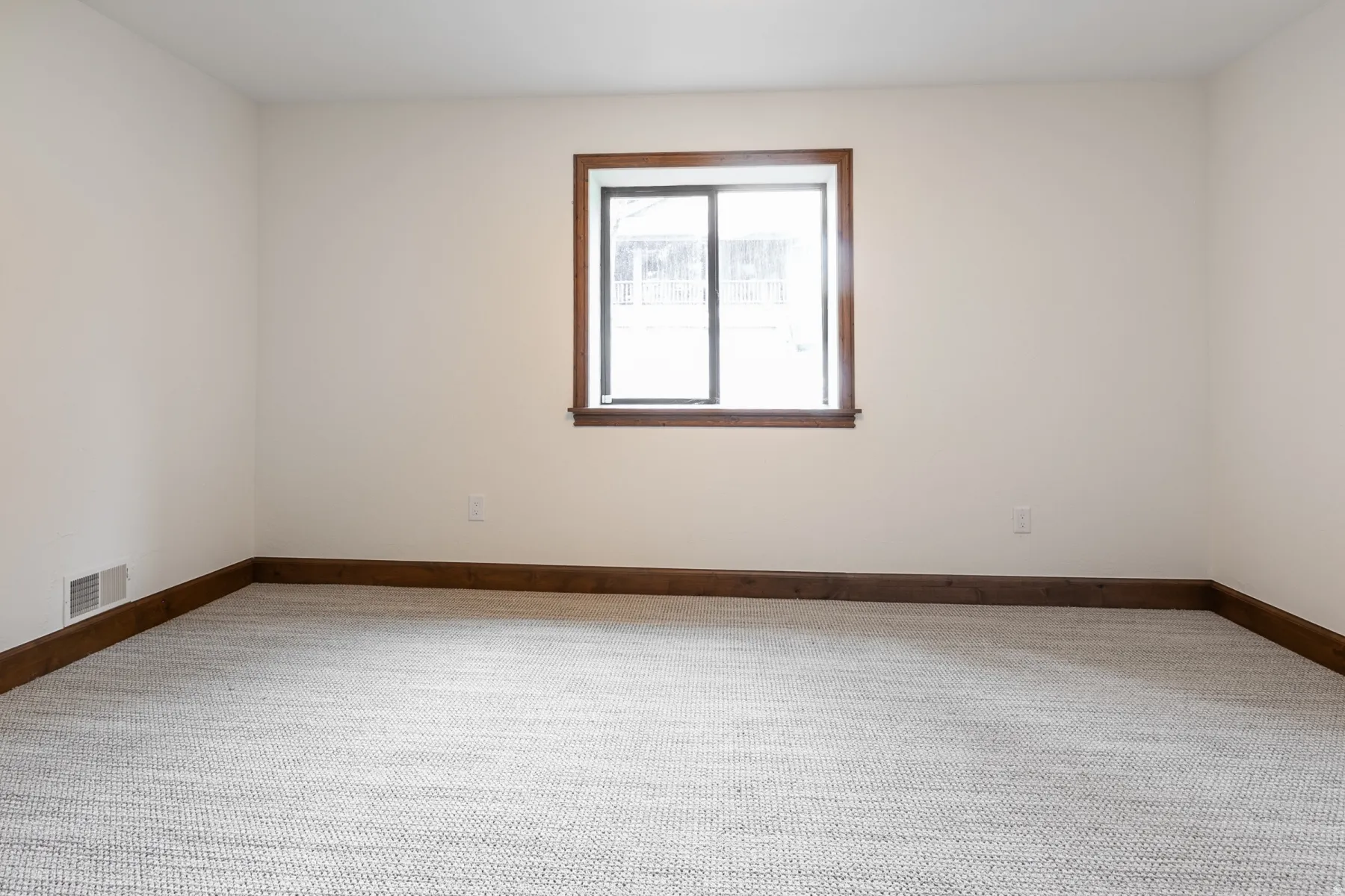 Bright room featuring a window with dark wood trim, light neutral walls, dark wood baseboards, and textured light gray carpet
