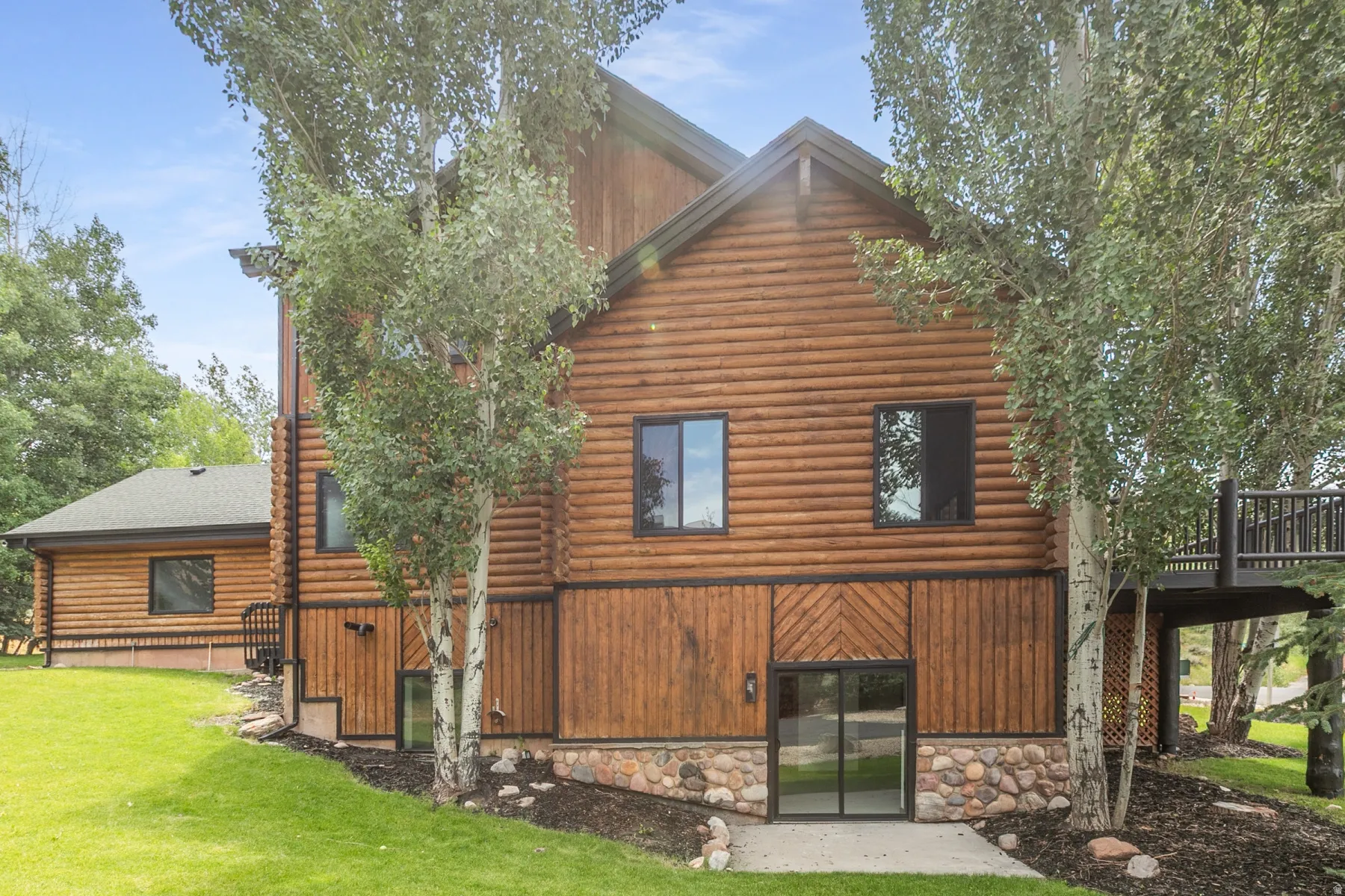 Log-style exterior featuring a stone foundation, black-framed windows, and a multi-level deck