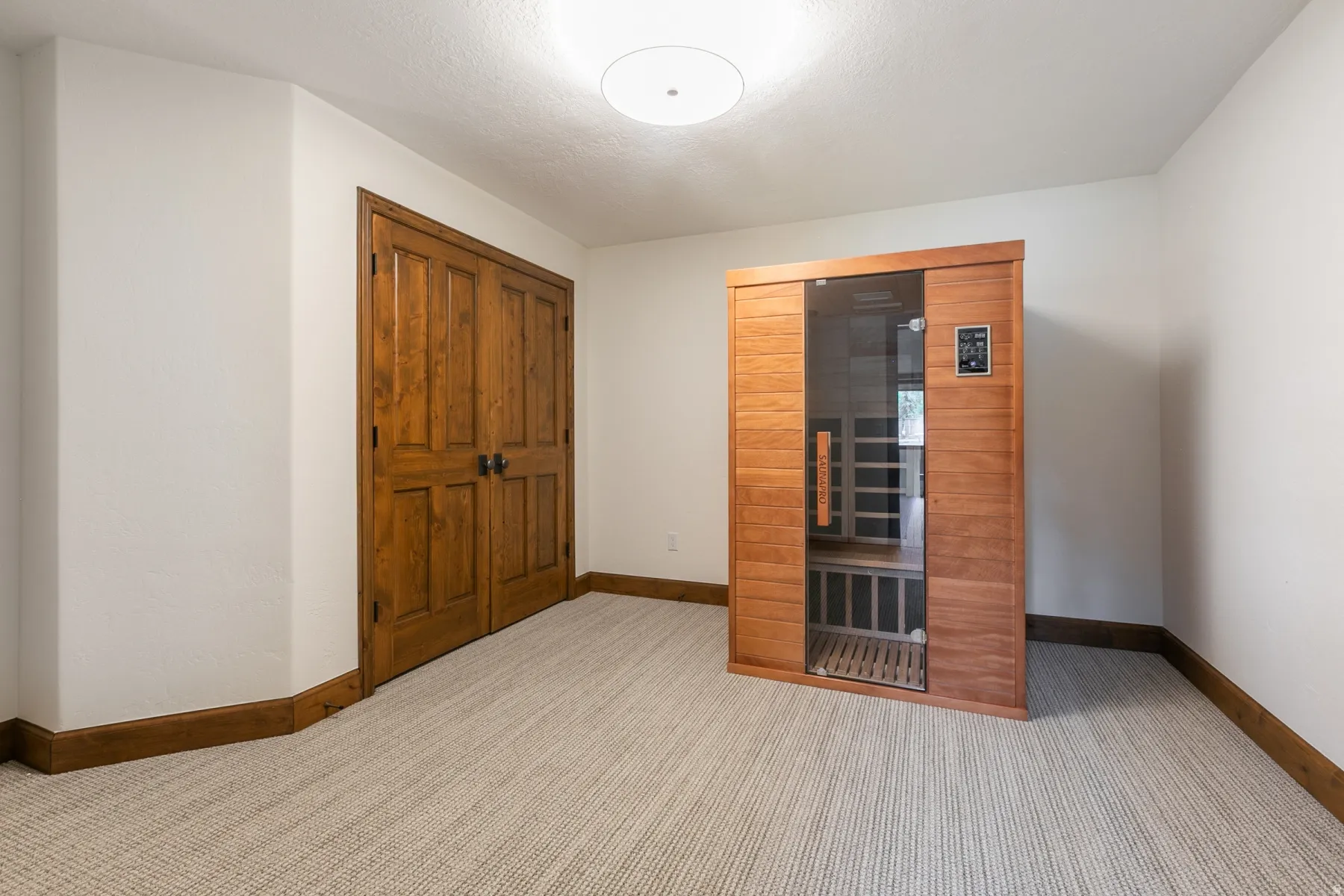Dedicated room featuring a built-in sauna with a glass door, light wood paneling, and an integrated control panel