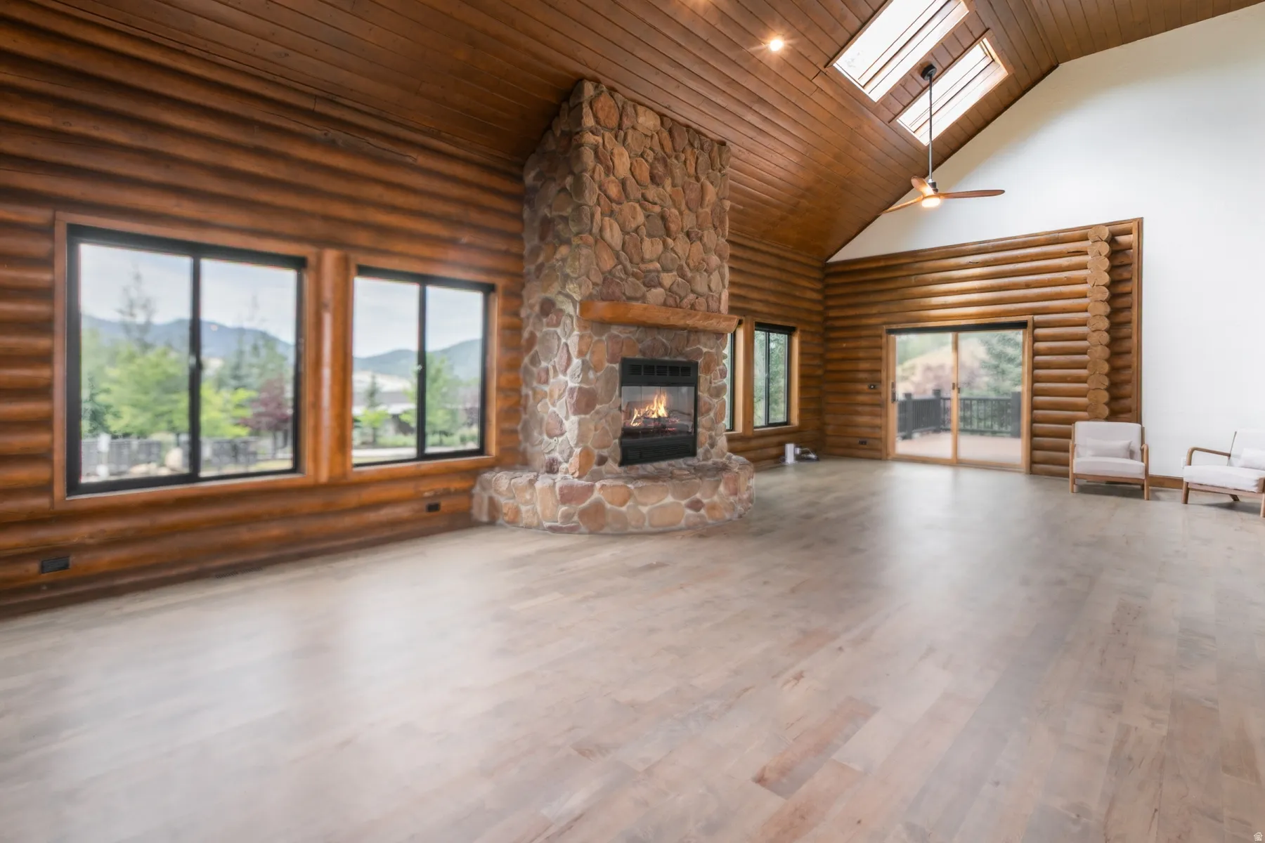 Expansive living area featuring a prominent stone fireplace, wood-finish flooring, and log walls