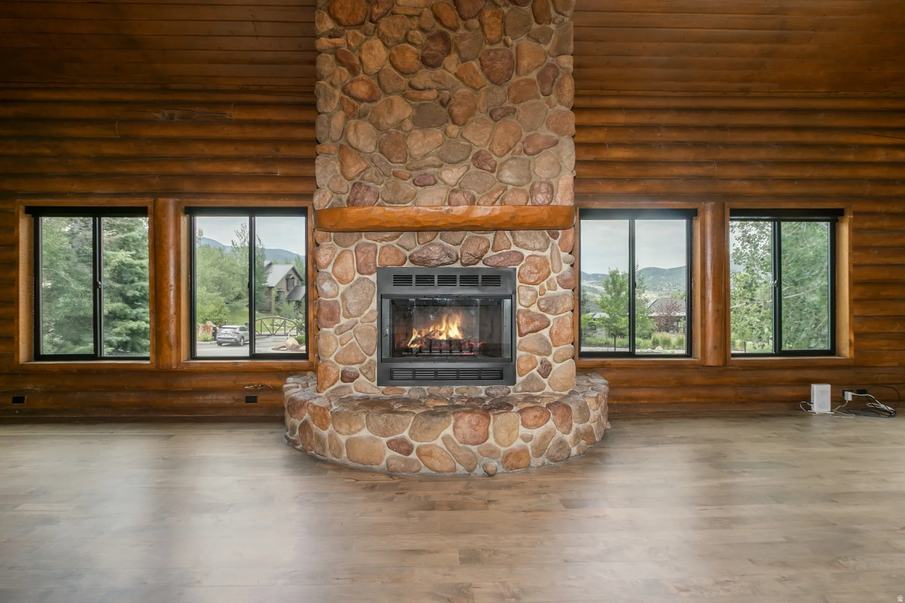 Stone fireplace with a wood mantel and hearth, flanked by two windows with black frames