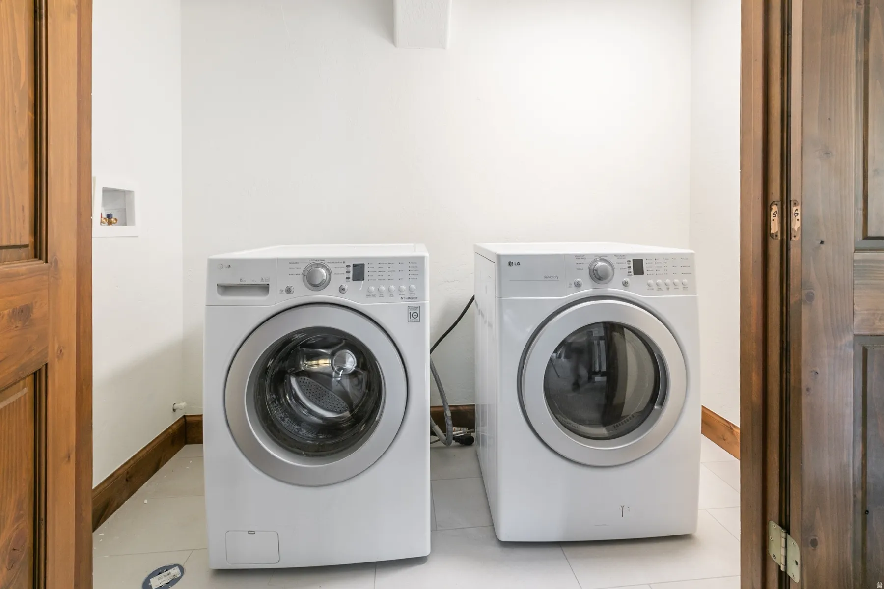 Dedicated laundry space featuring white tile flooring, white walls, and wood-finish trim