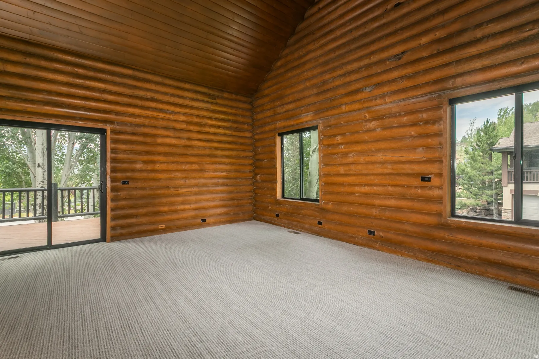 Spacious interior featuring natural log walls, a vaulted wood-plank ceiling, and light-colored carpeting