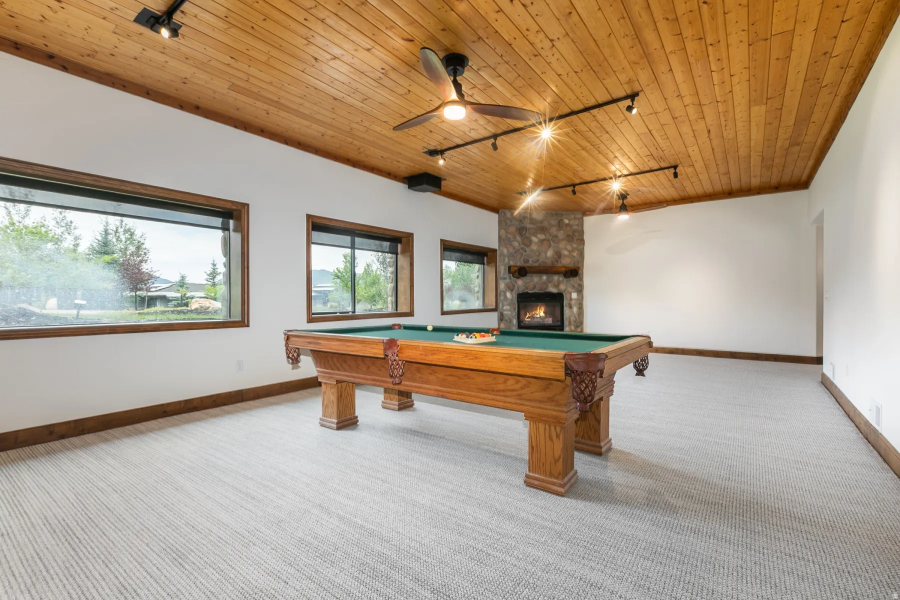 Recreational space featuring a stone fireplace with a wood mantle, wood-paneled ceiling, ceiling fan, and track lighting