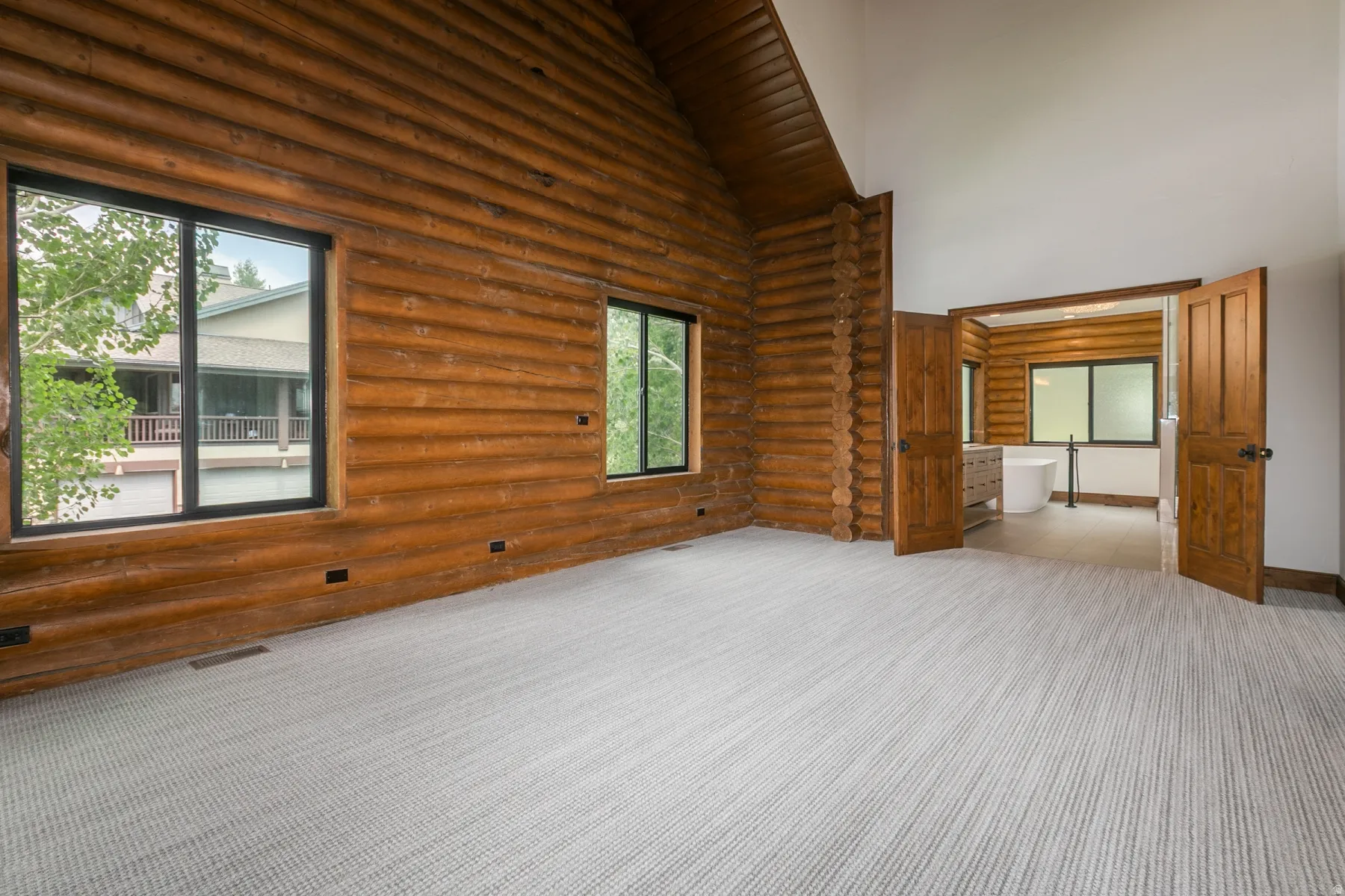 Spacious room featuring log wall construction, vaulted ceiling, and light-toned patterned carpet