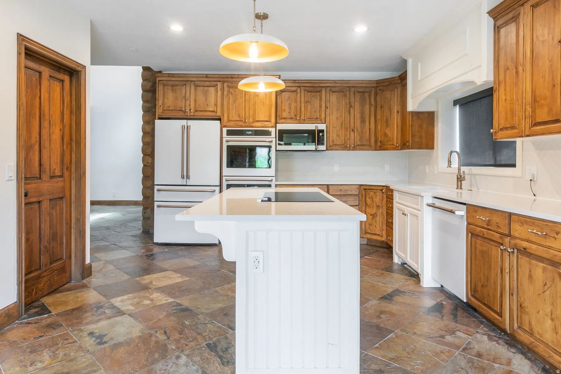 Kitchen featuring a white center island with a built-in cooktop, light wood cabinetry, white appliances, and a tiled backsplash