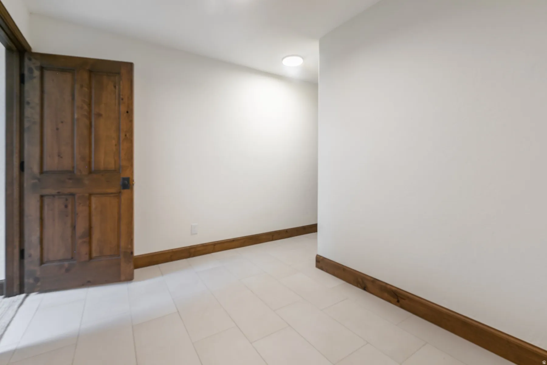 Panel wood door with dark hardware, white wall finishes, rich wood-finish baseboards, recessed lighting, and light tile flooring