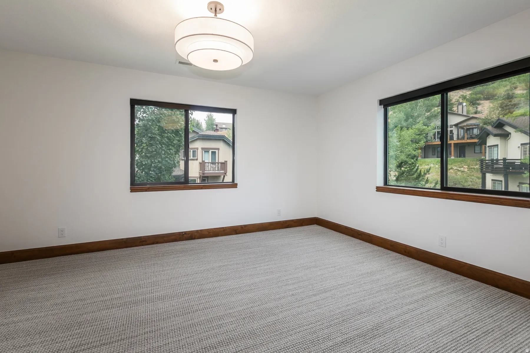 Spacious room featuring white walls, textured carpeting, and dark wood-tone baseboards