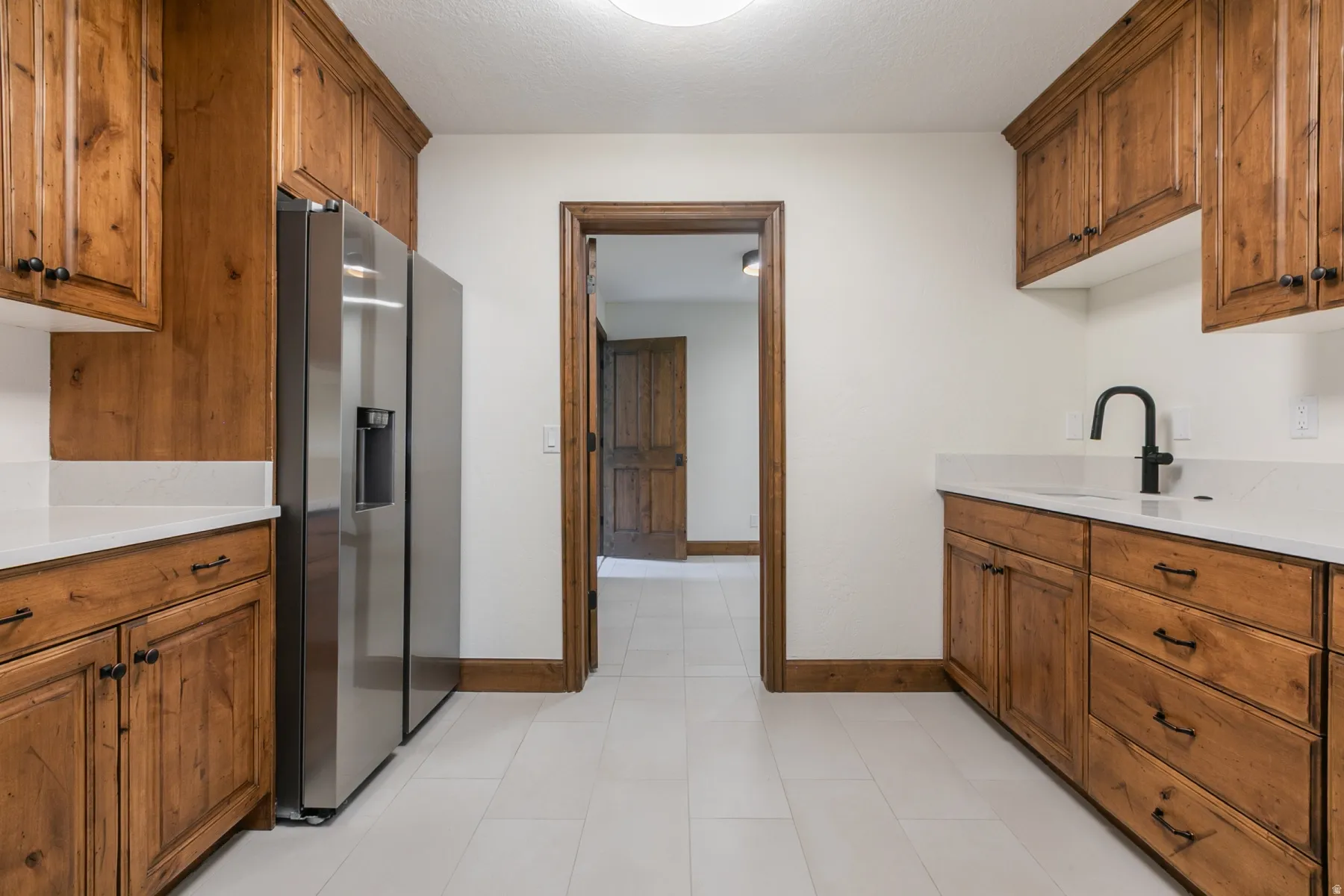 Kitchen featuring white tile flooring, custom wood cabinetry with black hardware, light countertops, and a stainless steel refrigerator