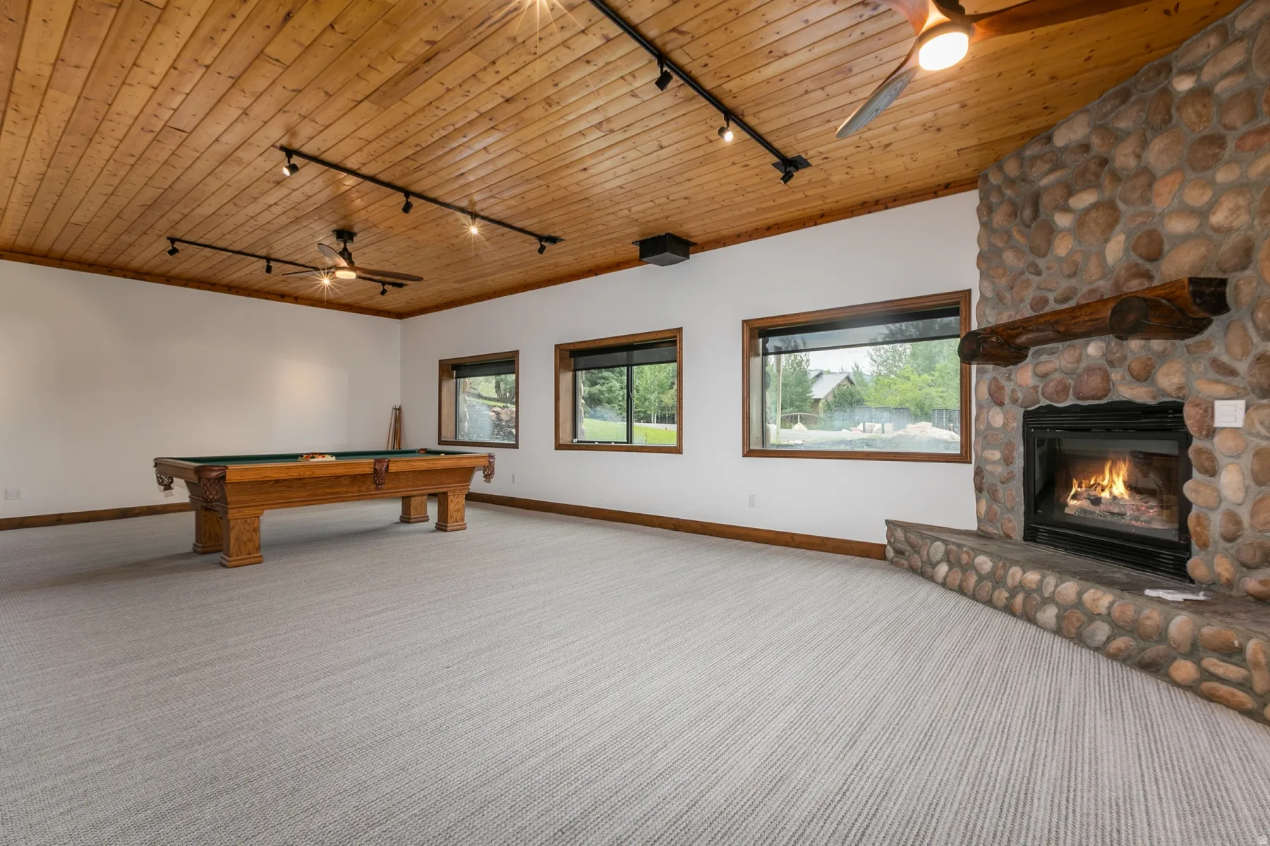 Spacious room featuring a stone-clad fireplace with a wood mantle, a wood-paneled ceiling, and multiple windows